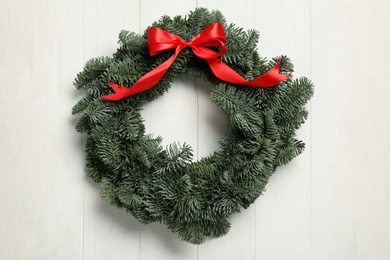 Photo of Christmas wreath made of fir tree branches with red ribbon on white wooden background