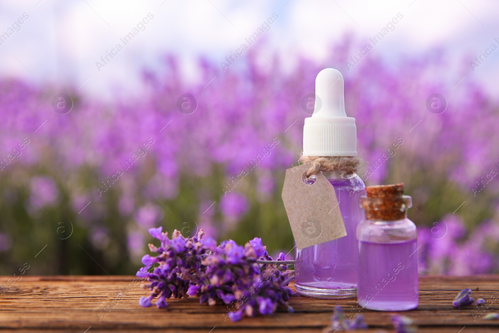 Photo of Bottles of natural essential oil and lavender flowers on wooden table. Space for text