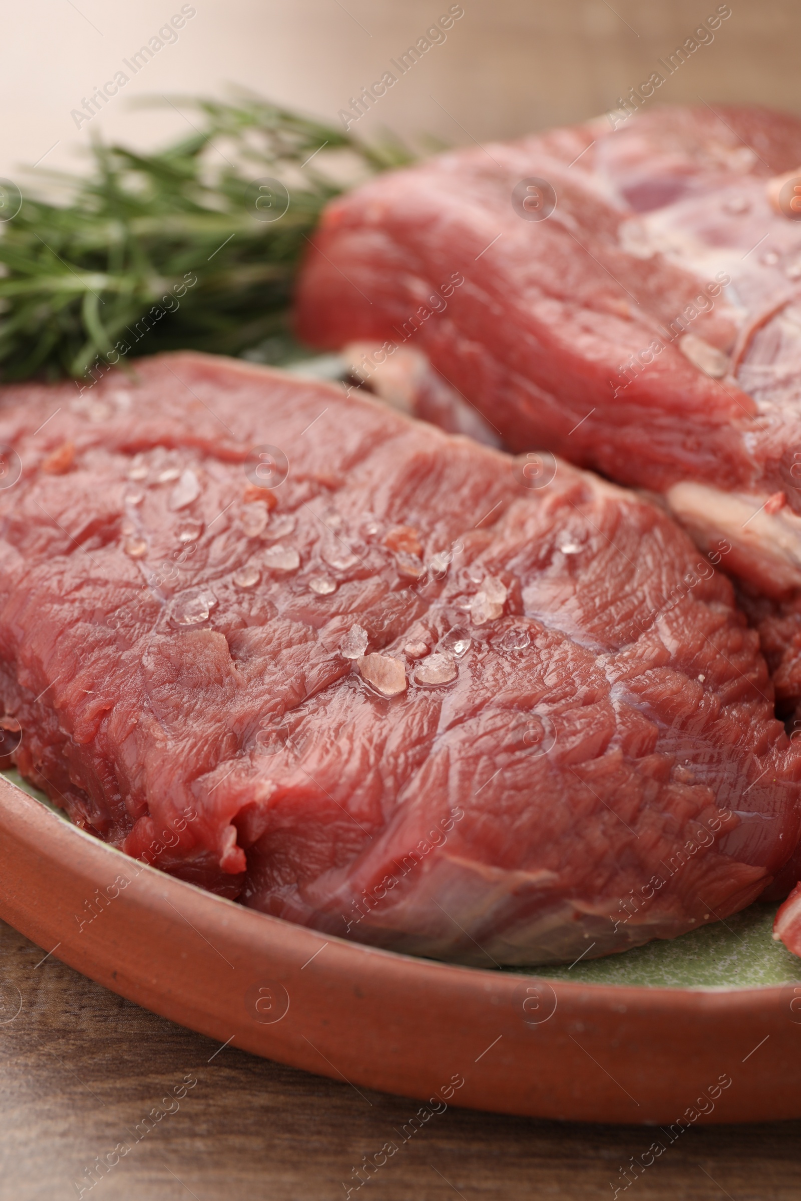 Photo of Pieces of raw beef meat with spices and rosemary on table, closeup