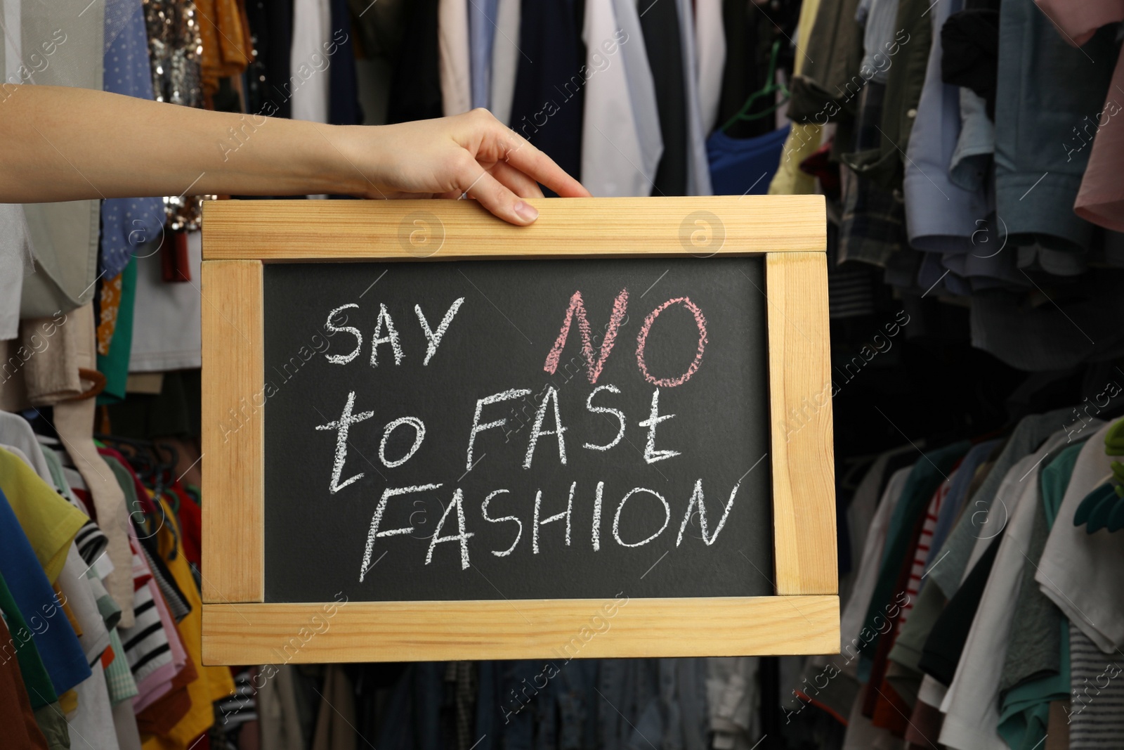 Photo of Woman holding small chalkboard with phrase SAY NO TO FAST FASHION in clothes store, closeup