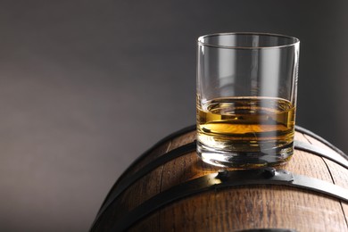 Whiskey in glass on wooden barrel against gray background, space for text