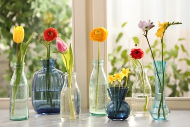 Photo of Different beautiful spring flowers in glassware on window sill