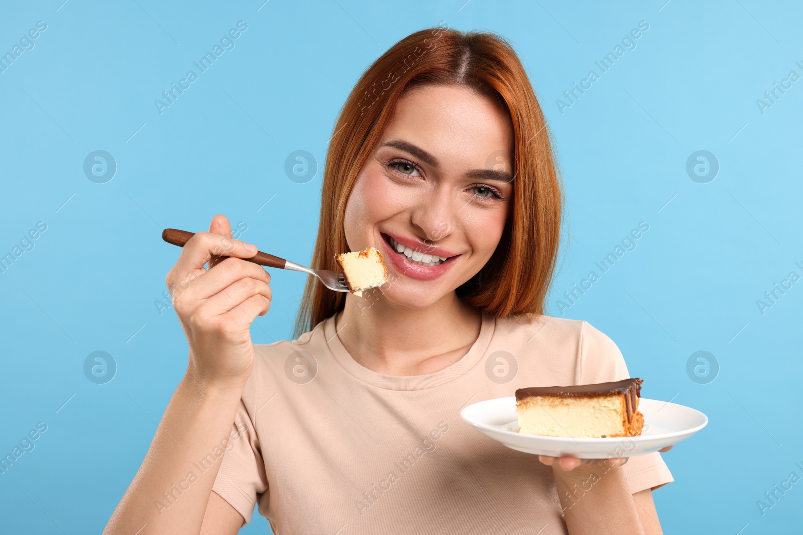 Photo of Young woman eating piece of tasty cake on light blue background