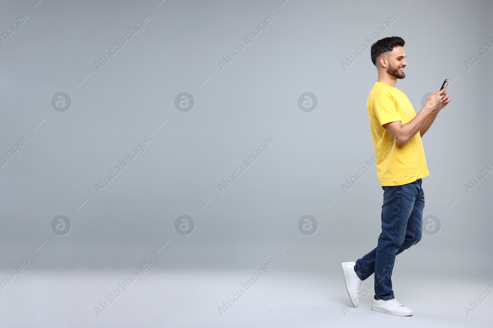 Photo of Happy young man using smartphone on grey background, space for text