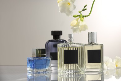 Luxury perfumes and freesia flowers on mirror surface against light grey background. Floral fragrance