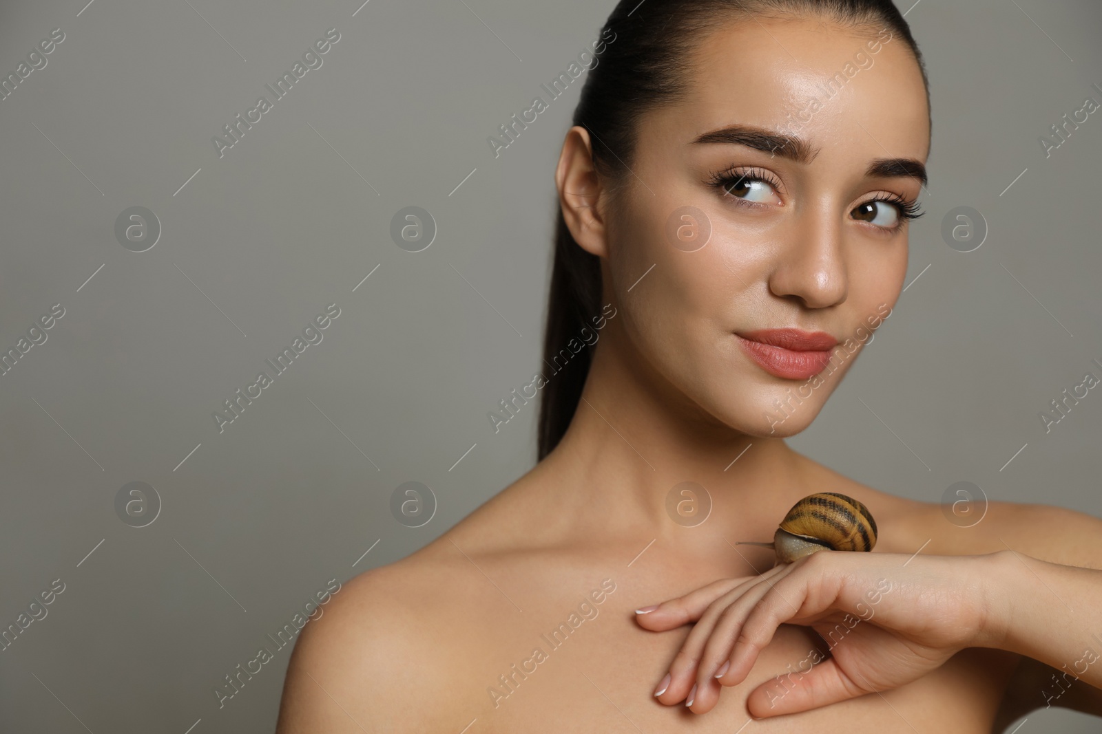 Photo of Beautiful young woman with snail on her hand against grey background. Space for text