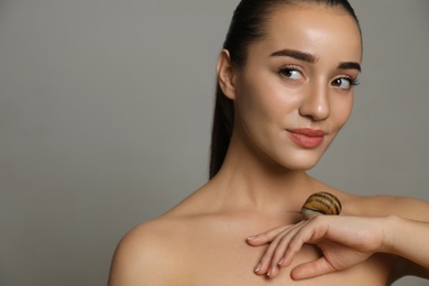 Photo of Beautiful young woman with snail on her hand against grey background. Space for text