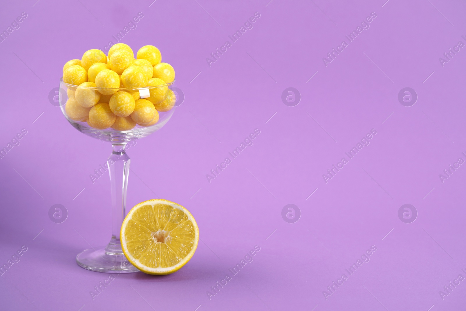 Photo of Tasty yellow chewing gums and lemon on purple background. Space for text