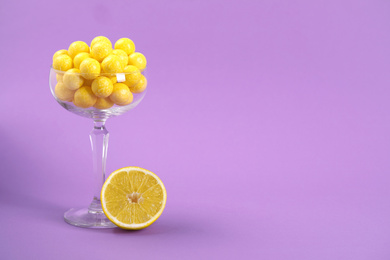 Photo of Tasty yellow chewing gums and lemon on purple background. Space for text