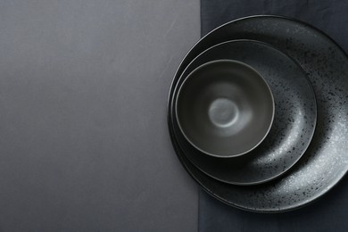 Stylish ceramic plates, bowl and napkin on grey background, top view. Space for text