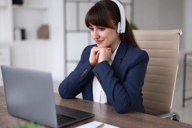 Woman in headphones watching webinar at wooden table in office