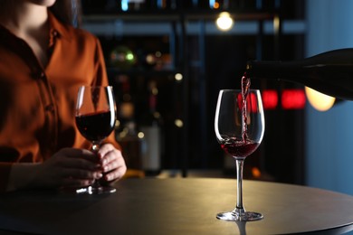 Photo of Pouring red wine from bottle into glass on table indoors