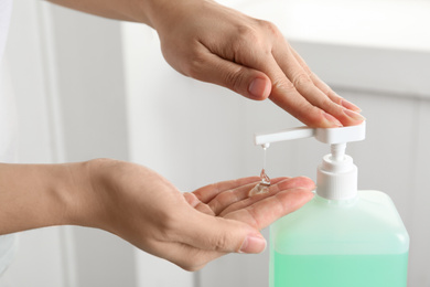 Photo of Woman applying antiseptic gel on hand indoors, closeup