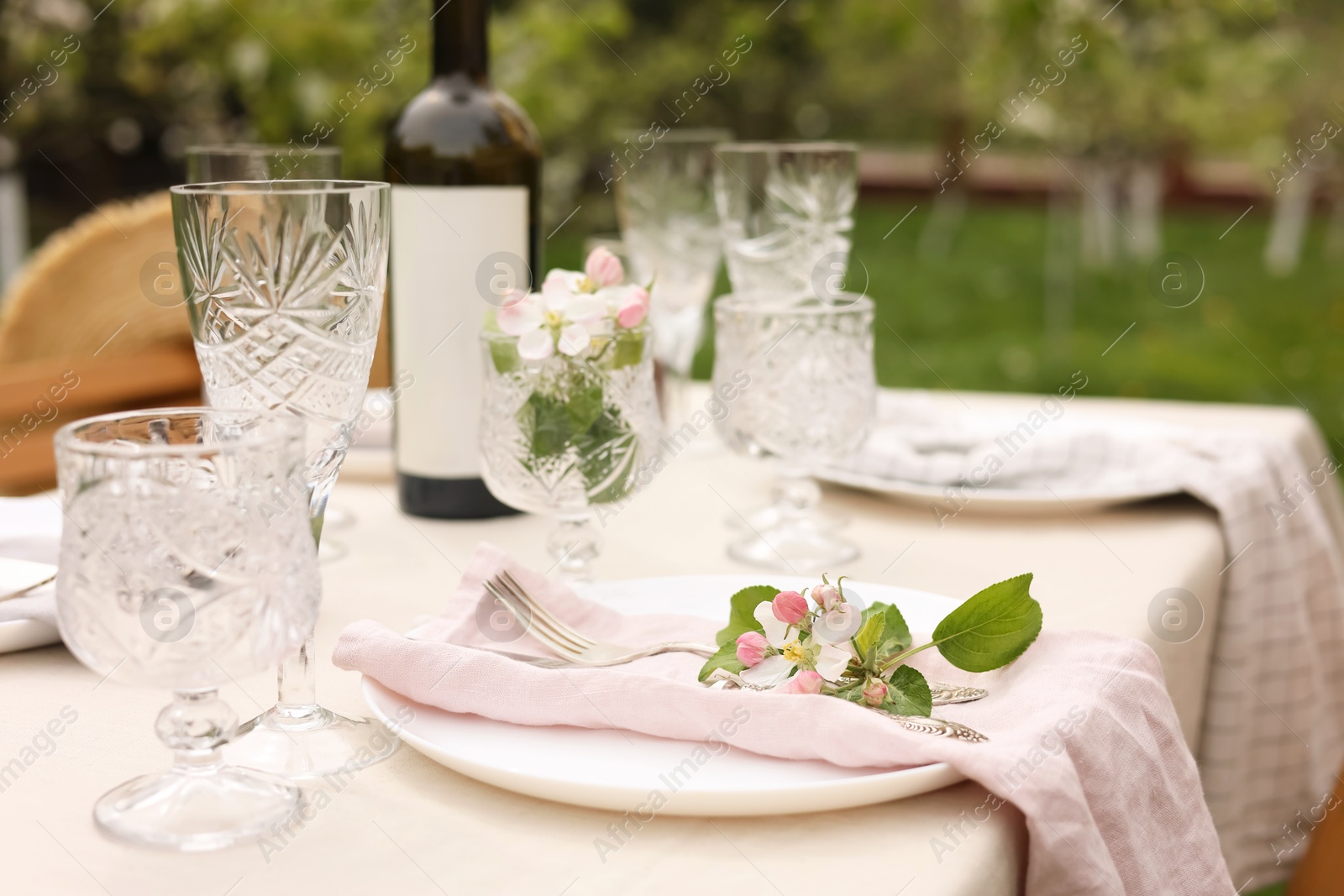 Photo of Stylish table setting with beautiful spring flowers, wine, plates and glasses in garden