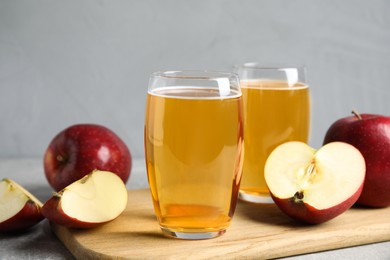 Delicious cider and ripe red apples on grey table