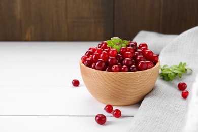 Photo of Fresh ripe cranberries and branches on white wooden table, space for text