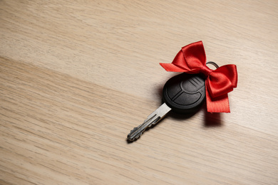 Photo of Key with red bow on wooden background, space for text. Car buying