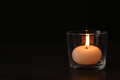 Photo of Burning candle in glass holder on table against dark background, space for text