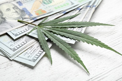 Photo of Hemp leaf and dollars on white wooden background, closeup