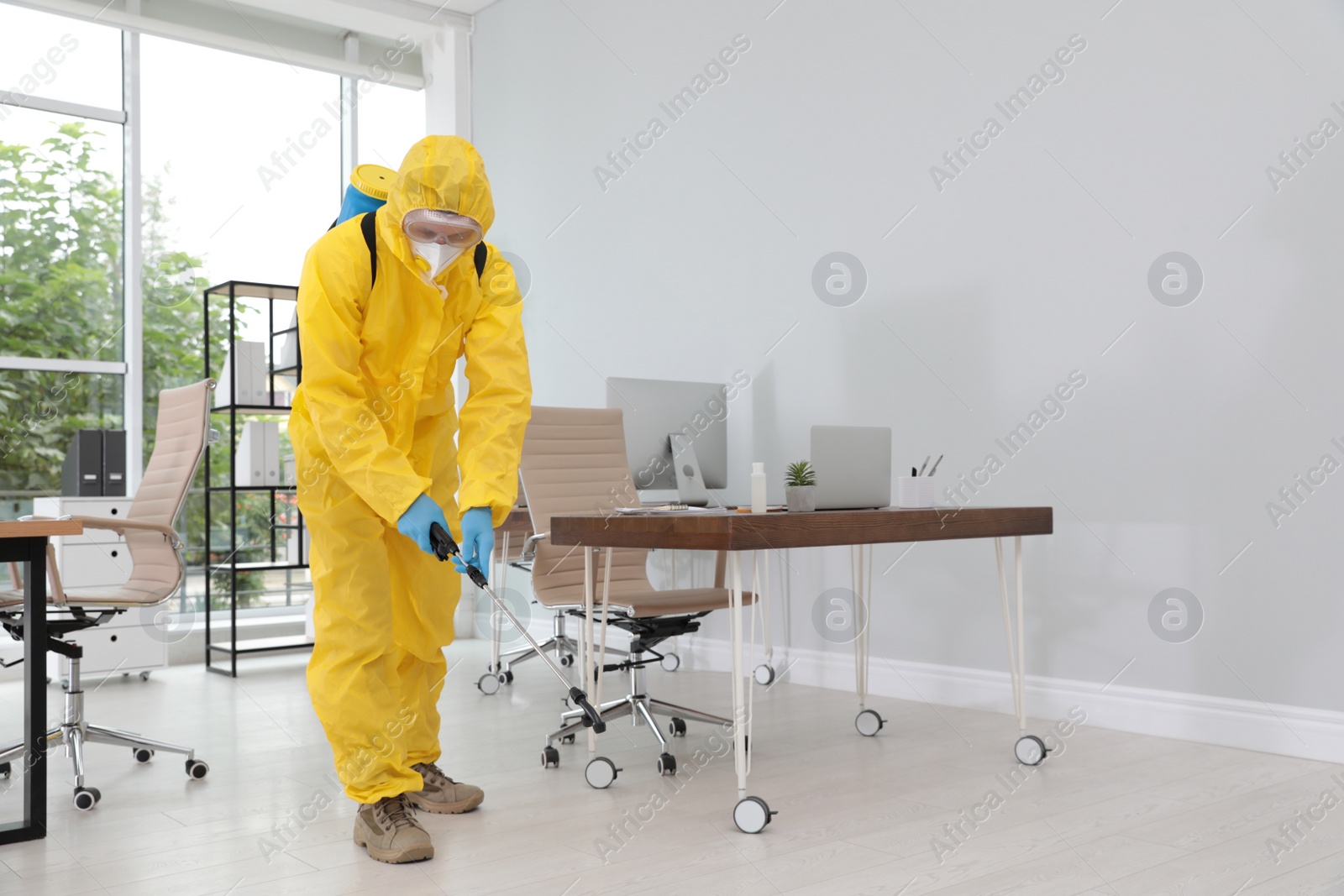 Photo of Janitor in protective suit disinfecting office to prevent spreading of COVID-19