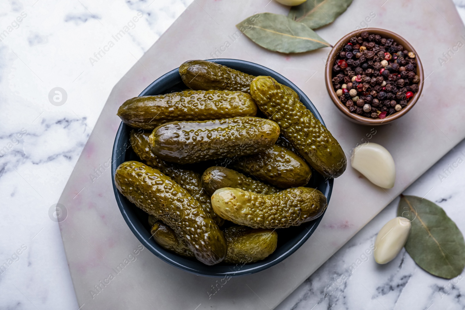 Photo of Bowl of pickled cucumbers and ingredients on white marble table, flat lay