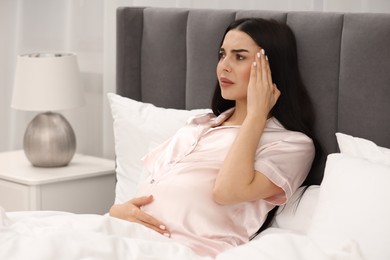 Photo of Pregnant woman suffering from headache in bed at home