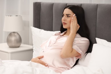 Pregnant woman suffering from headache in bed at home