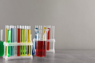 Photo of Test tubes with liquids in stand and flasks on table against light grey background, space for text