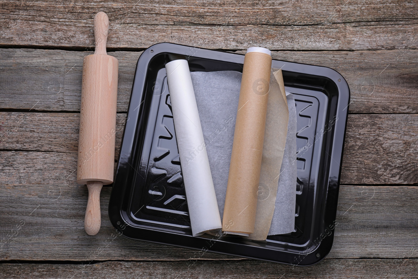 Photo of Rolls of parchment paper in baking pan and rolling pin on wooden table, flat lay