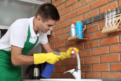 Photo of Man cleaning tap with rag in kitchen