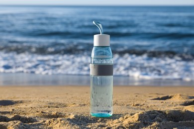 Photo of Glass bottle with water on wet sand near sea