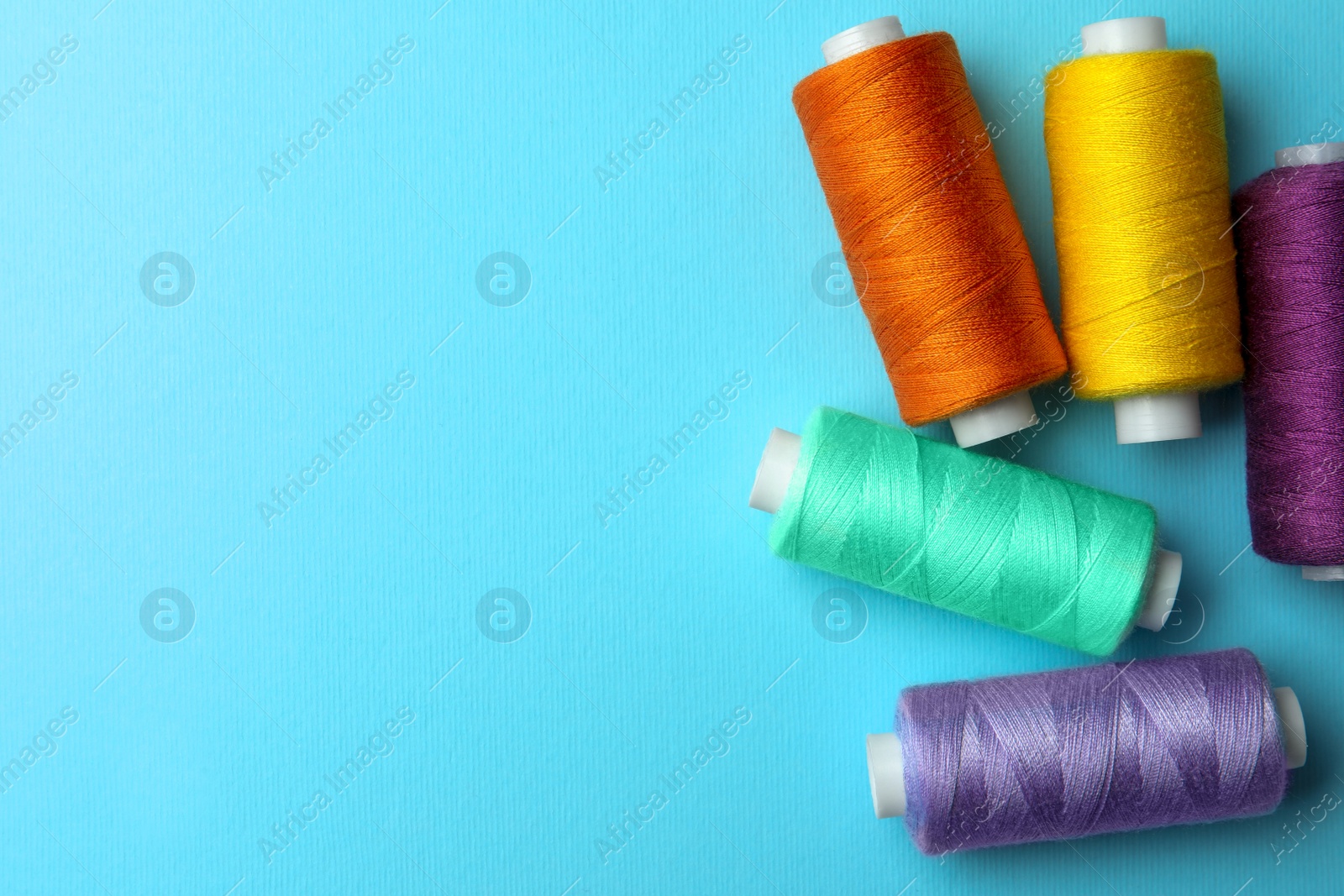 Photo of Different colorful sewing threads on light blue background, flat lay. Space for text