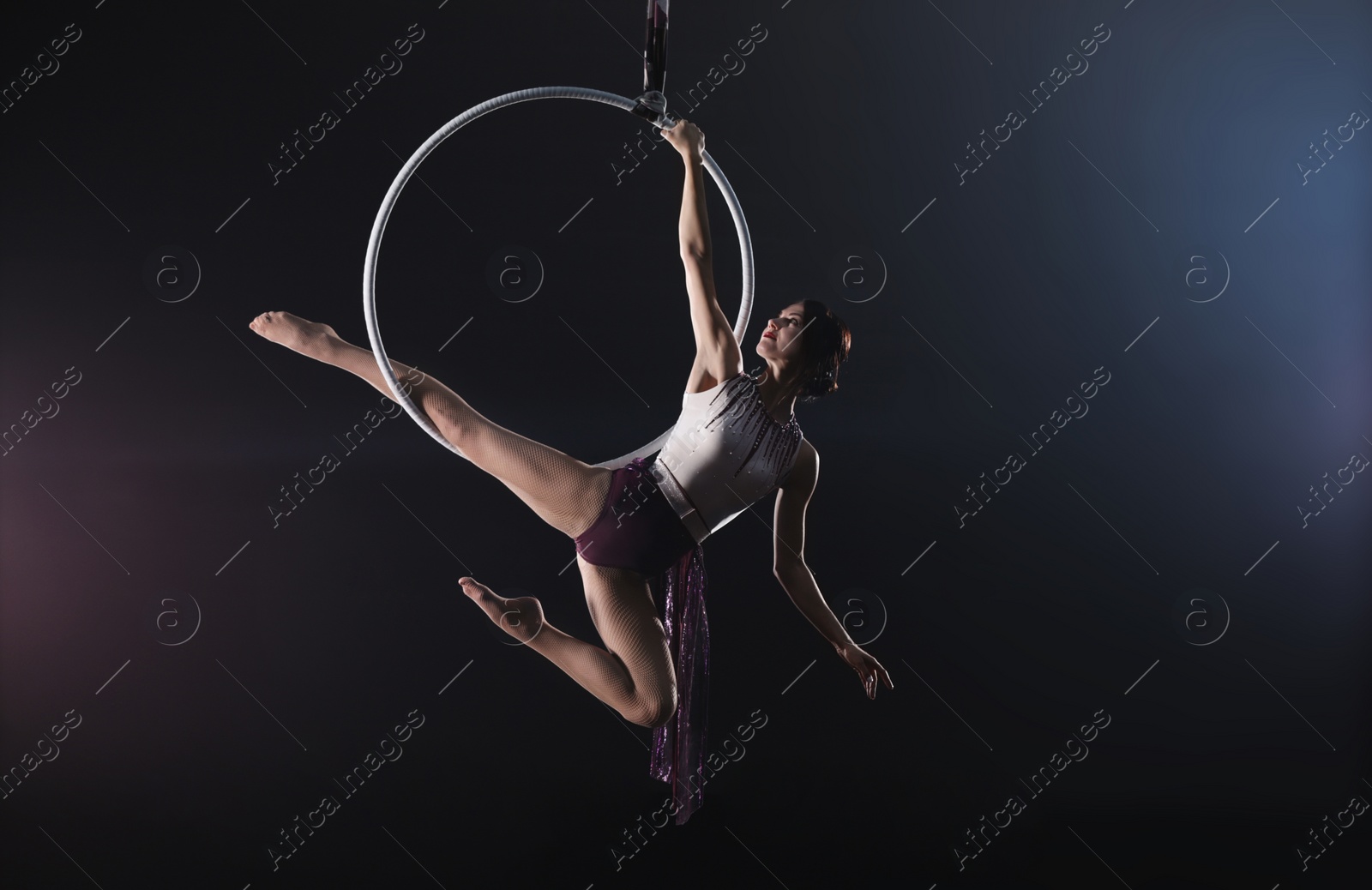 Photo of Young woman performing acrobatic element on aerial ring indoors