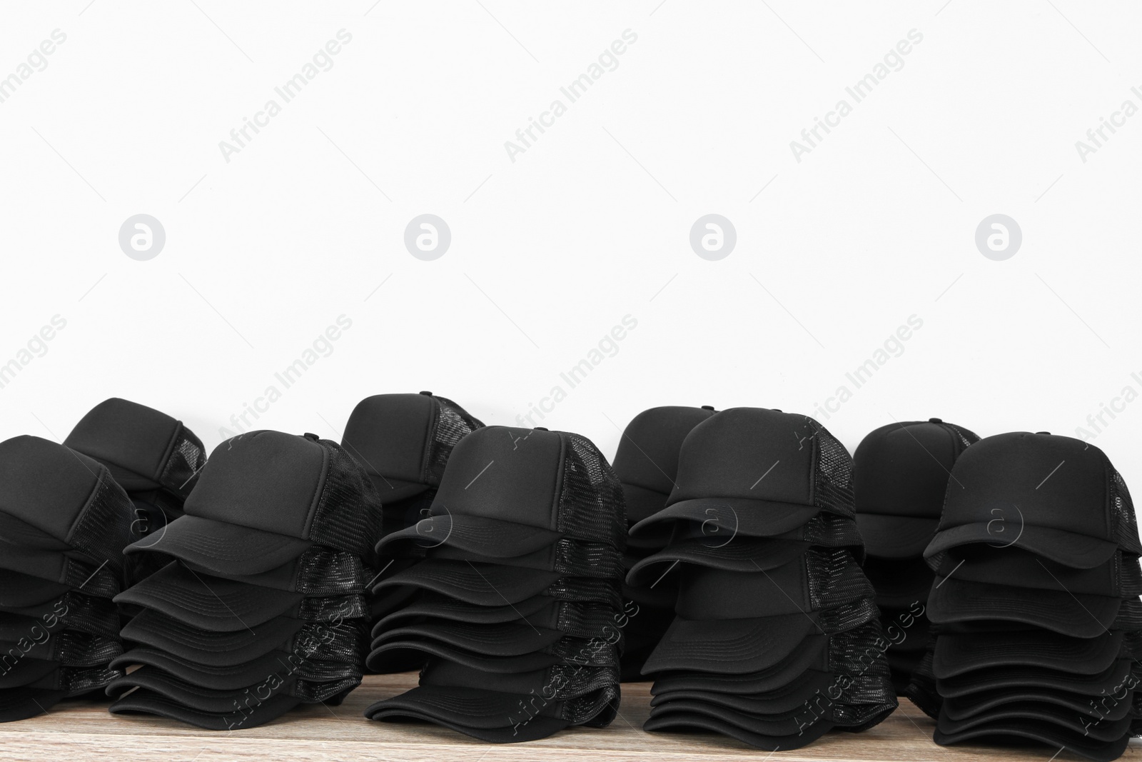 Photo of Many blank black caps on wooden table near light wall. Mock up for design