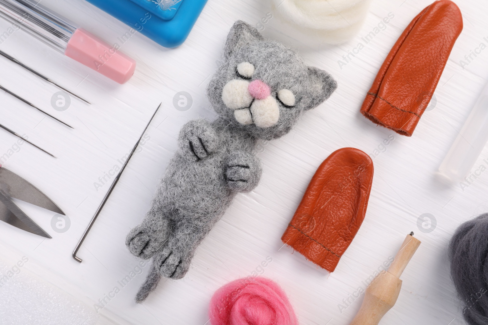 Photo of Felted cat, wool and different tools on white wooden table, flat lay