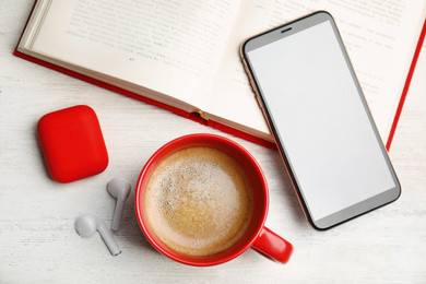 Photo of Book, coffee, earphones and mobile phone on white wooden table, flat lay