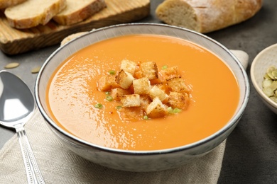 Photo of Tasty creamy pumpkin soup with croutons in bowl on grey table