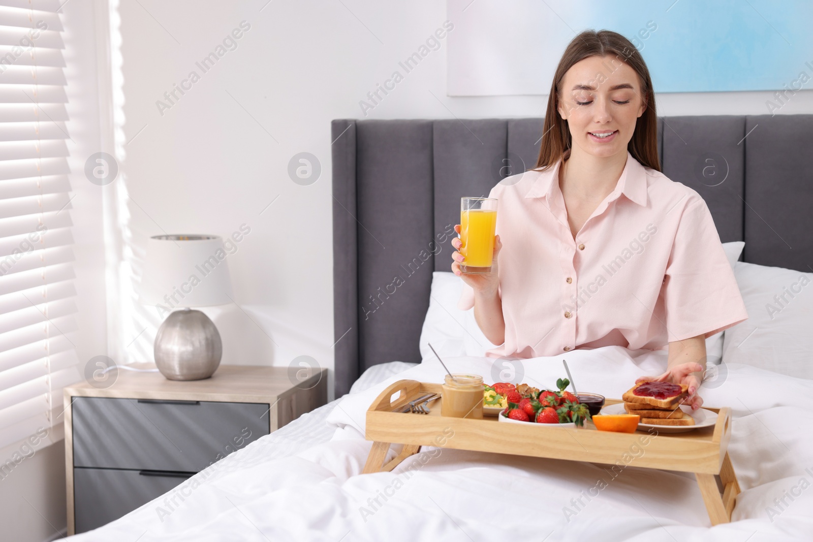 Photo of Smiling woman having breakfast in bed at home. Space for text