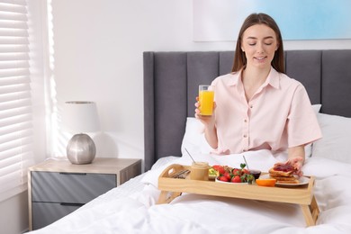 Smiling woman having breakfast in bed at home. Space for text