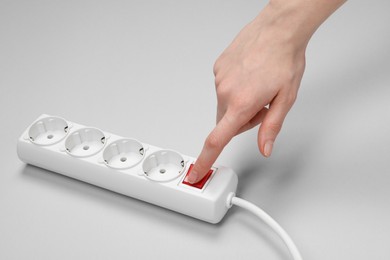 Photo of Woman pressing switch button of power strip on white background, closeup