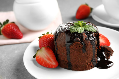Photo of Delicious warm chocolate lava cake with mint and strawberries on table, closeup