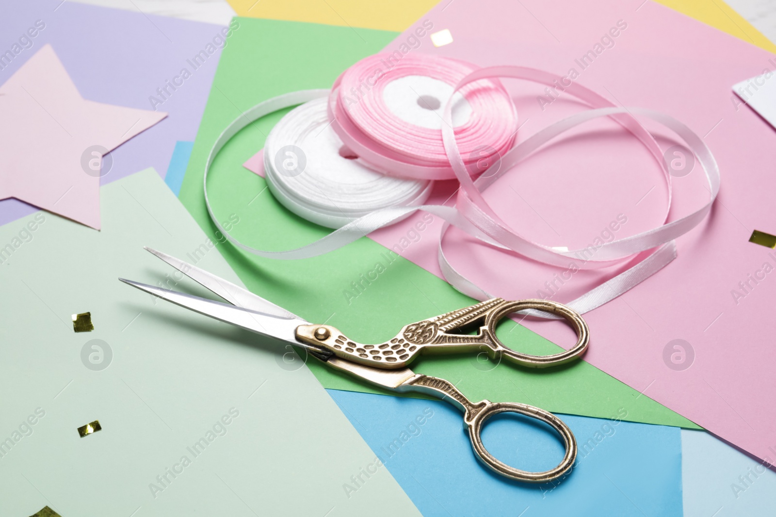 Photo of Pair of scissors near ribbons on colorful paper sheets, closeup