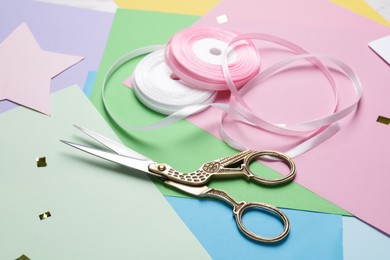 Pair of scissors near ribbons on colorful paper sheets, closeup