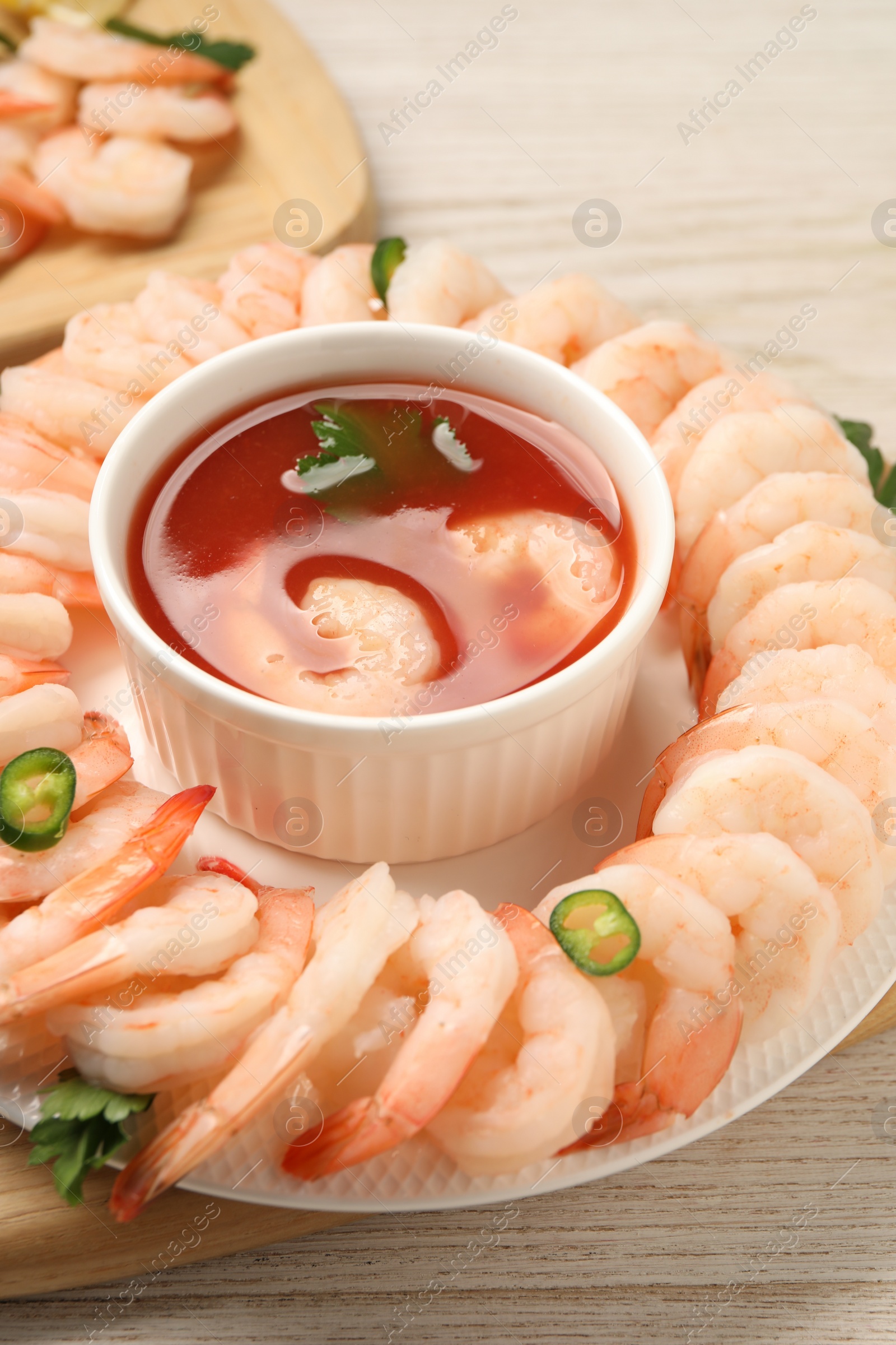 Photo of Tasty boiled shrimps with cocktail sauce, chili and parsley on light wooden table, closeup