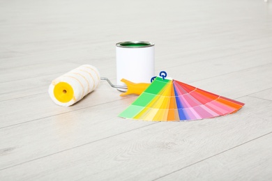 Can of paint, roller brush and color palette on wooden floor indoors