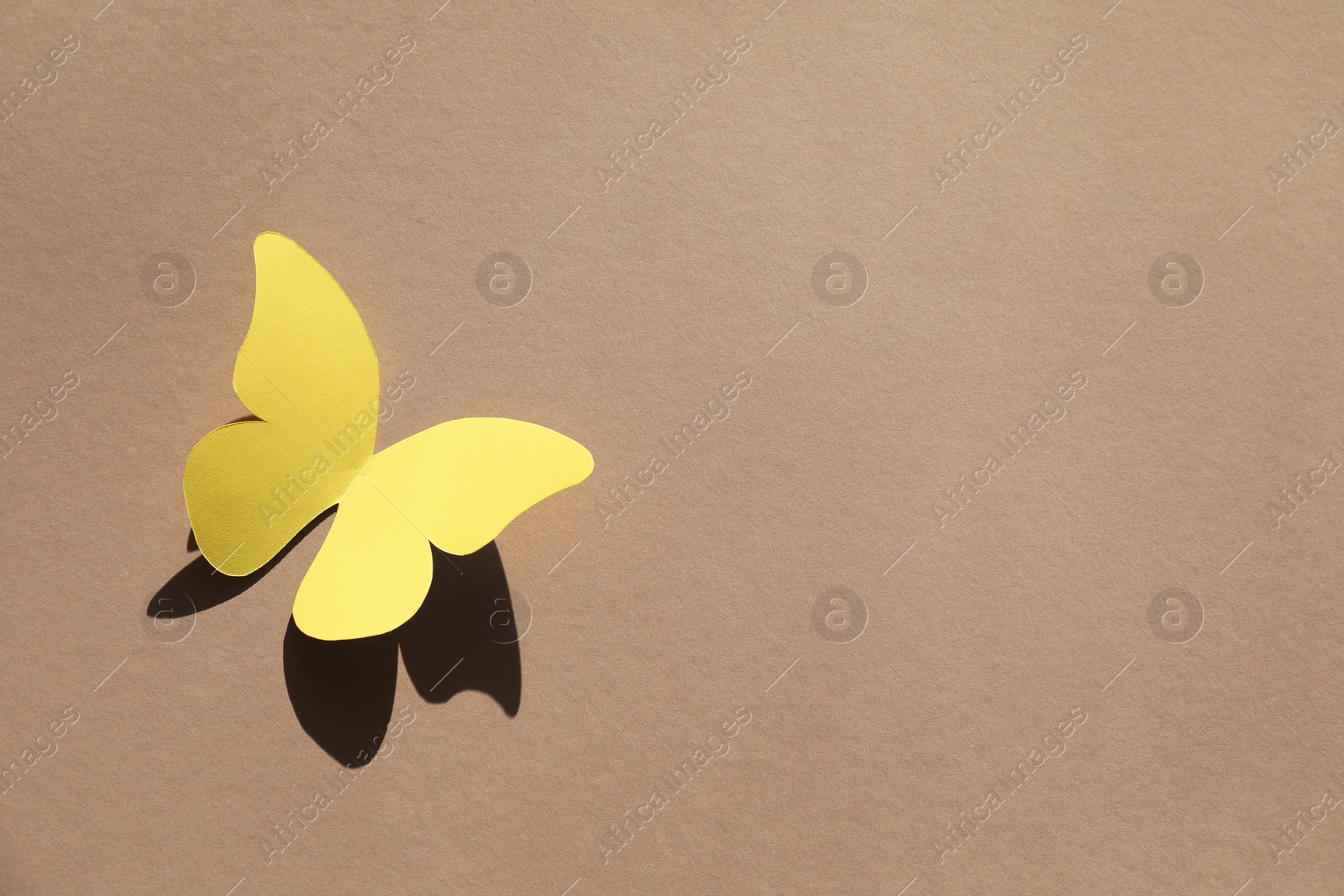 Photo of Yellow paper butterfly on light brown background, top view. Space for text