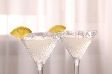 Photo of Elegant martini glasses with fresh cocktail and lemon slices near curtain
