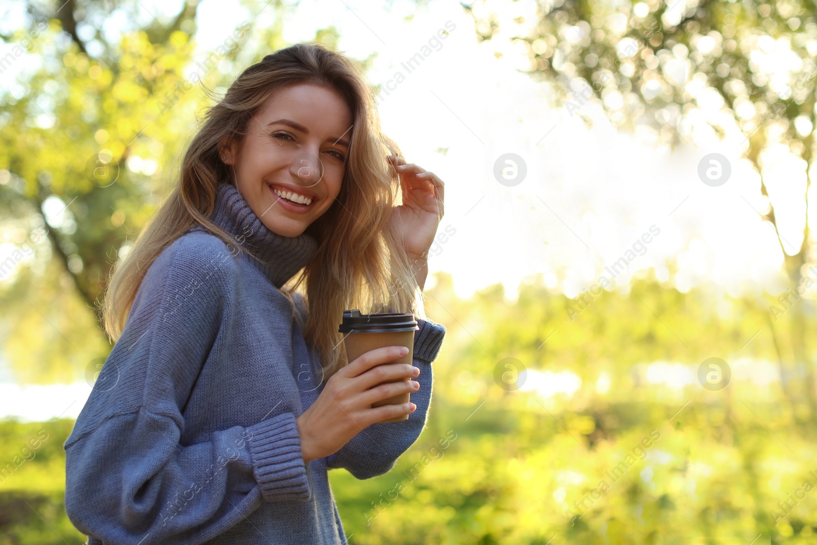 Photo of Beautiful young woman with coffee cup wearing stylish sweater in autumn park