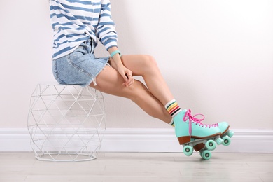 Young woman with retro roller skates near white wall, closeup