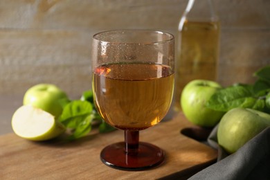 Glass of delicious cider and apples with green leaves on wooden table, closeup